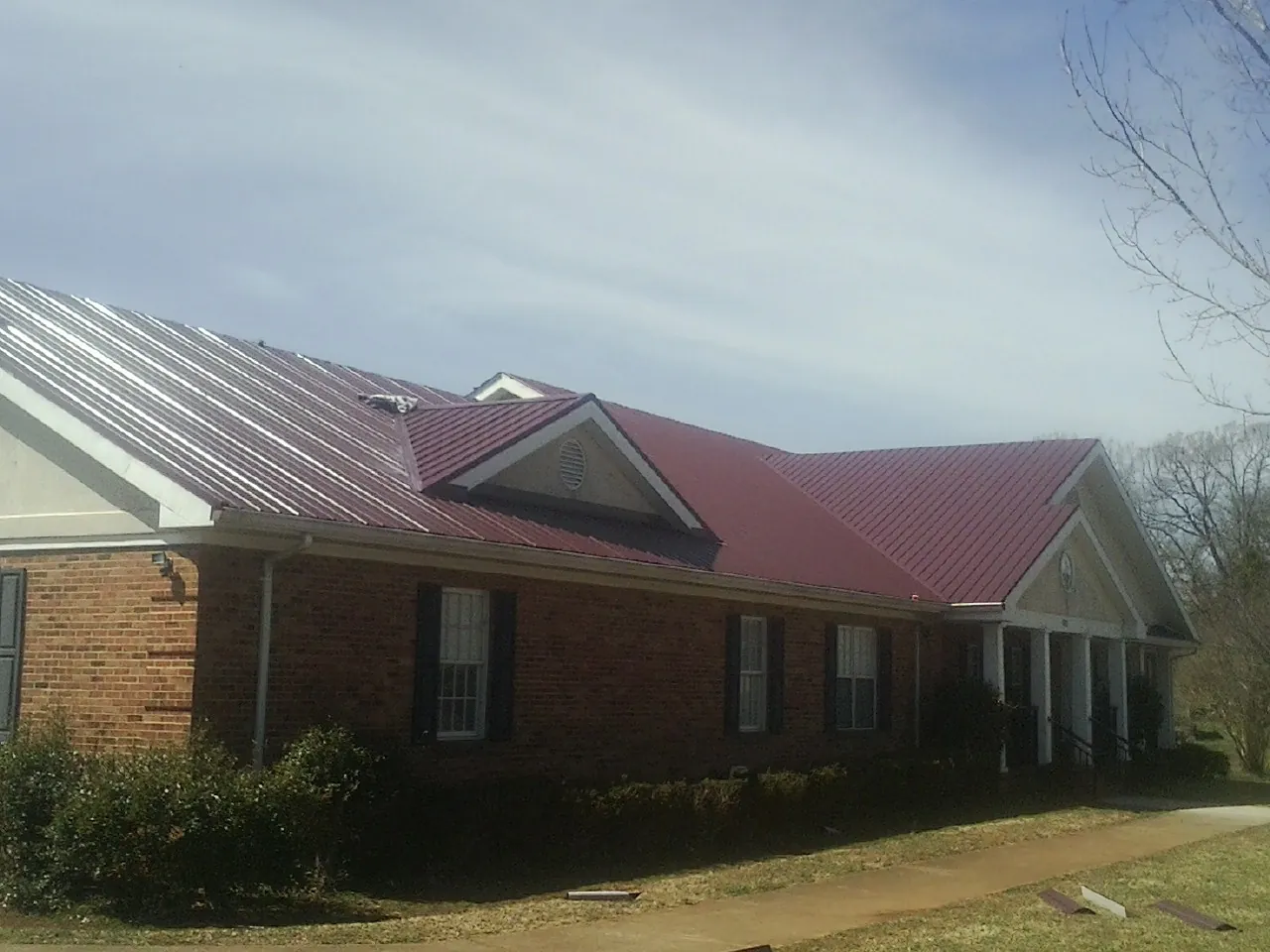 Red metal roof with gabled entries on a long brick building, from a Hail Damage Roof Repair job in Mentor