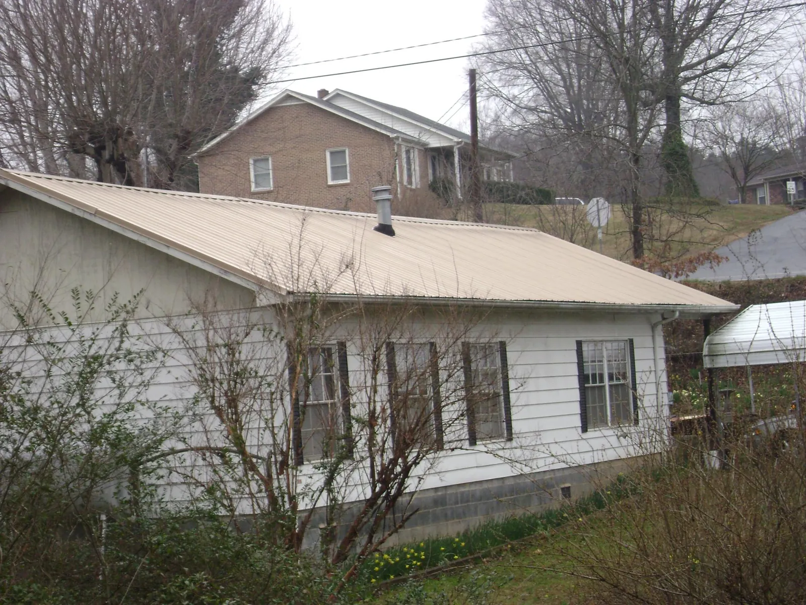 Tan metal roof on a white sided house set into a hillside — Commercial Roofing by Roofing Brothers in Mentor